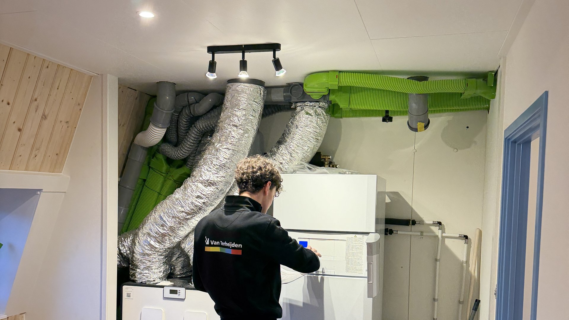 Monteur bij ventilatie- en warmtepomp-installatie op zolderverdieping, overzichtsshot