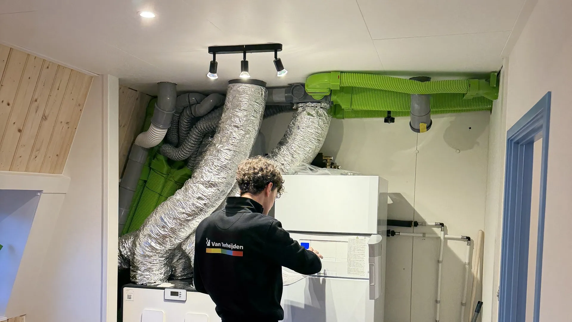 Monteur bij ventilatie- en warmtepomp-installatie op zolderverdieping, overzichtsshot