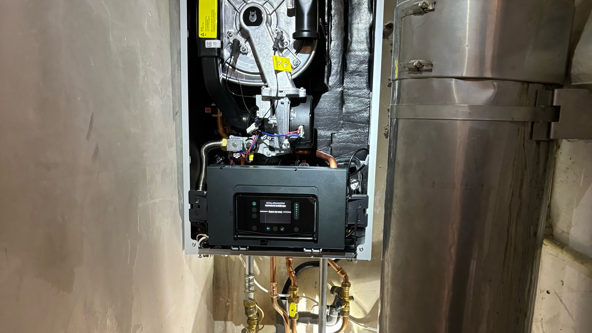 Cv-ketel open zonder frontpaneel in technische ruimte met leidingen en afvoer