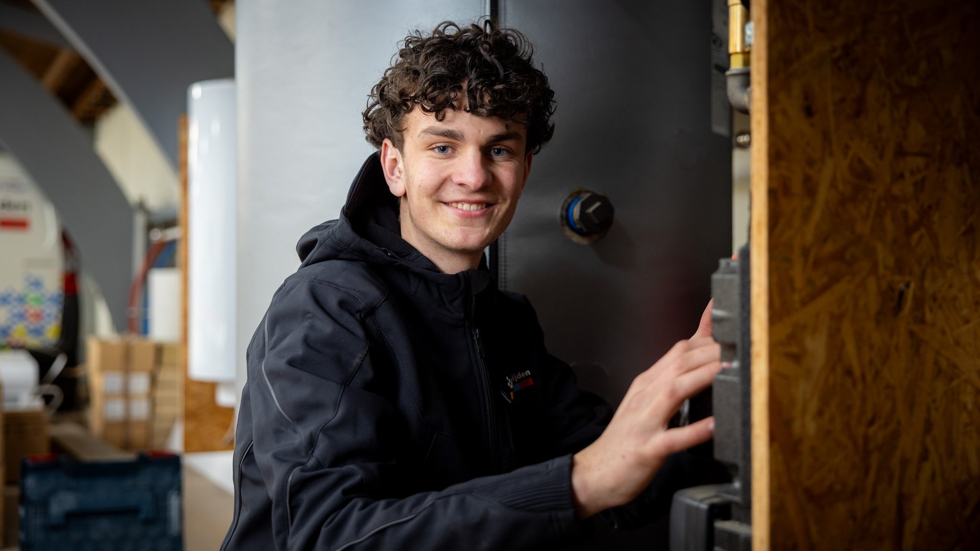 Lachende installatiemonteur naast warmtepomp-unit in werkplaats