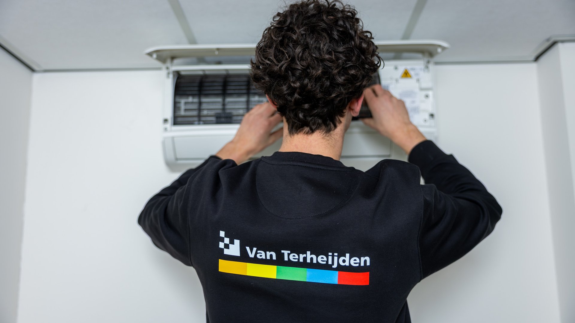 Monteur met Van Terheijden-logo op rug werkt aan airco