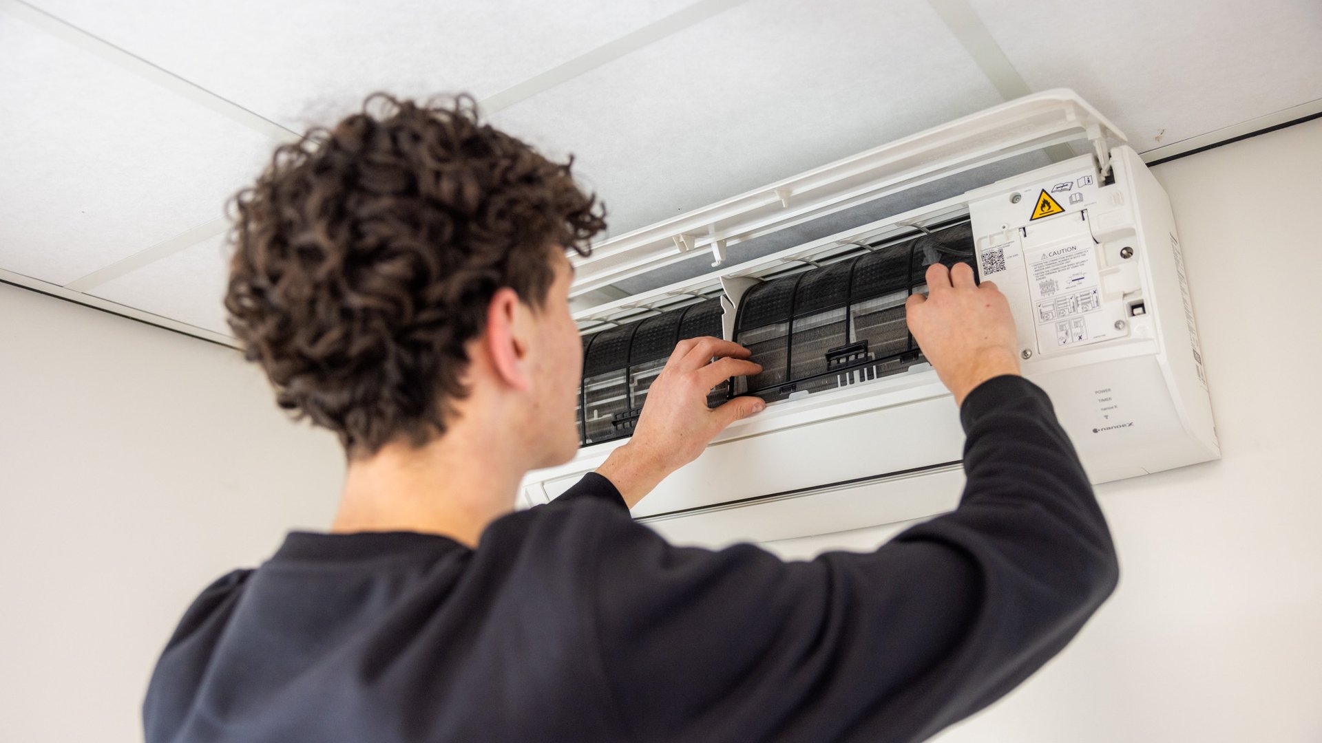 Monteur reinigt binnenkant van airco binnenunit tijdens onderhoud